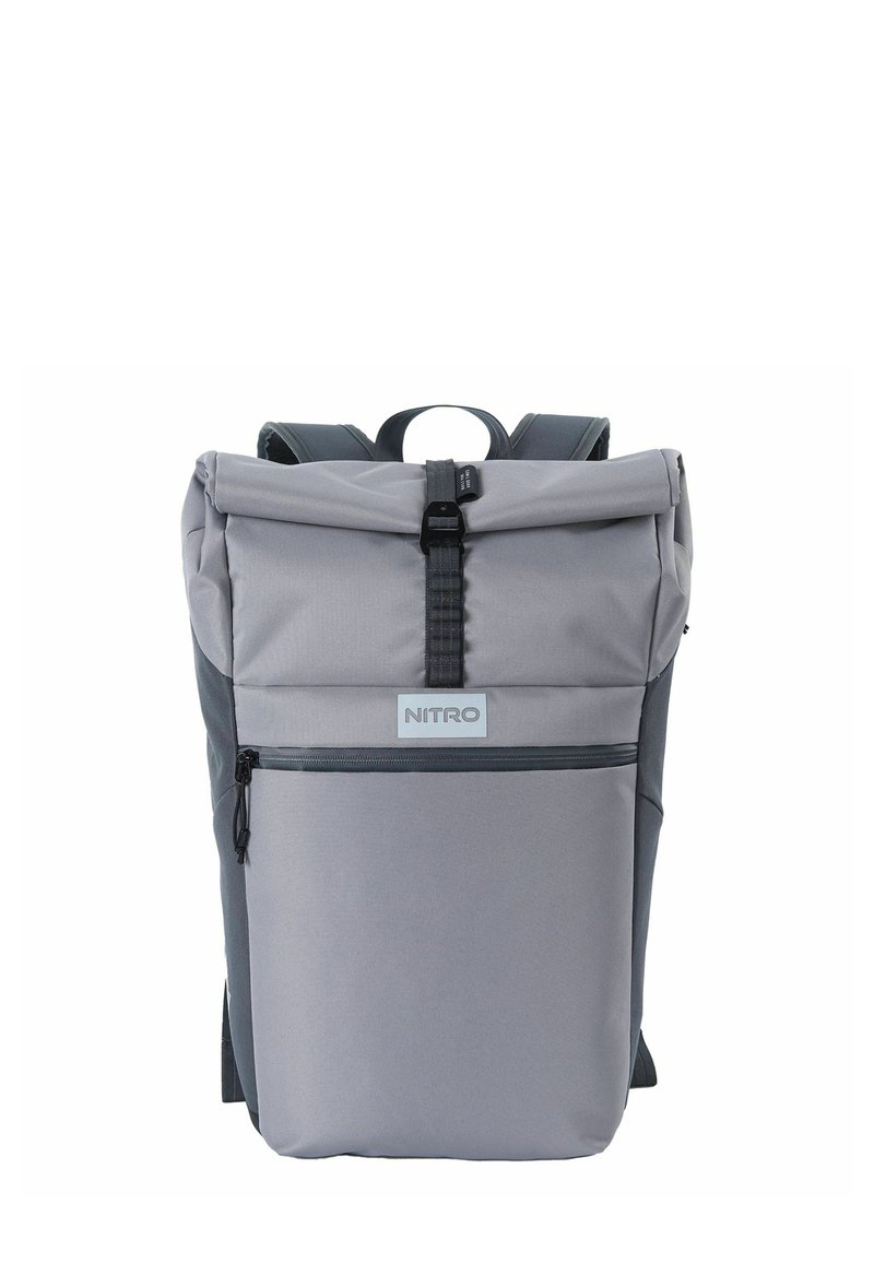 Sac à dos gris à rabat roulé en tissu durable, avec une poche zippée sur le devant, des bretelles ajustables et une étiquette de marque sur le panneau frontal.