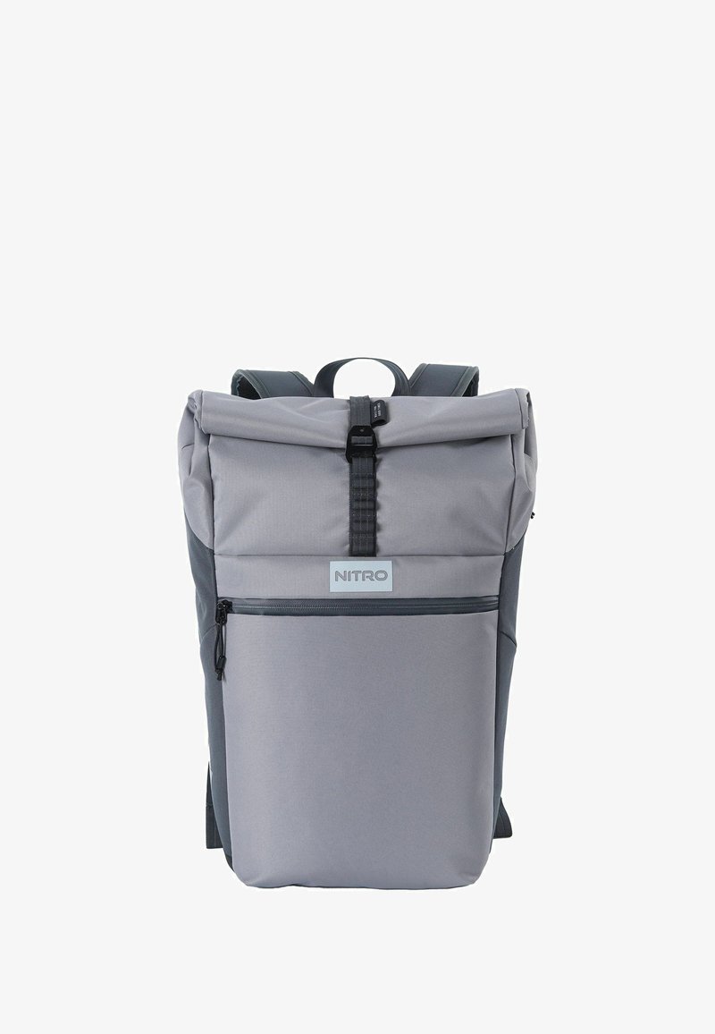 Sac à dos gris à rabat roulé en tissu durable, avec une poche zippée sur le devant, des bretelles ajustables et une étiquette de marque sur le panneau frontal.