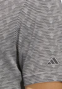 Gray and black striped T-shirt with a textured surface; features a subtle Adidas logo on the sleeve. Slightly fitted design, short sleeves.