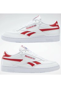 Fehér bőr sneaker piros kiegészítőkkel és fehér talppal. Jellemzői közé tartozik a fűző, a párnázott nyelv, valamint a logó az oldalon és a saroknál.
