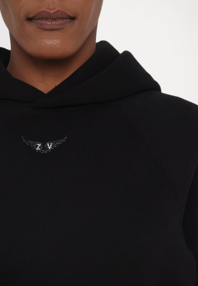 Svart hettegenser med rund hals, som har en liten metallisk rhinestone vinge-logo foran. Mykt stoff og ribbestrikkede detaljer.