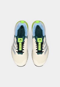 Baskets d'entraînement Adidas avec un dessus en mesh crème, accents turquoise et détails vert fluo. Lacets noirs et trois stries argentées.