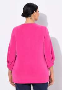 Maglia a maniche lunghe di un vivo colore rosa, presenta una vestibilità morbida, scollatura arrotondata e dettagli arricciati sulle maniche. Tessuto morbido e liscio.