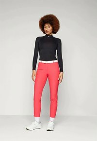 Zwarte lange mouwen top met hoge kraag, gecombineerd met roze aansluitende broek, witte riem en witte sneakers. Gladde stof, op maat gemaakt.