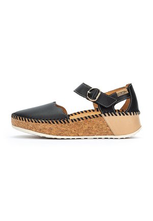 Chaussure en cuir noir avec un semelle en liège, présentant un bout rond et une sangle ajustable avec une boucle métallique. Des coutures mettent en valeur le design.