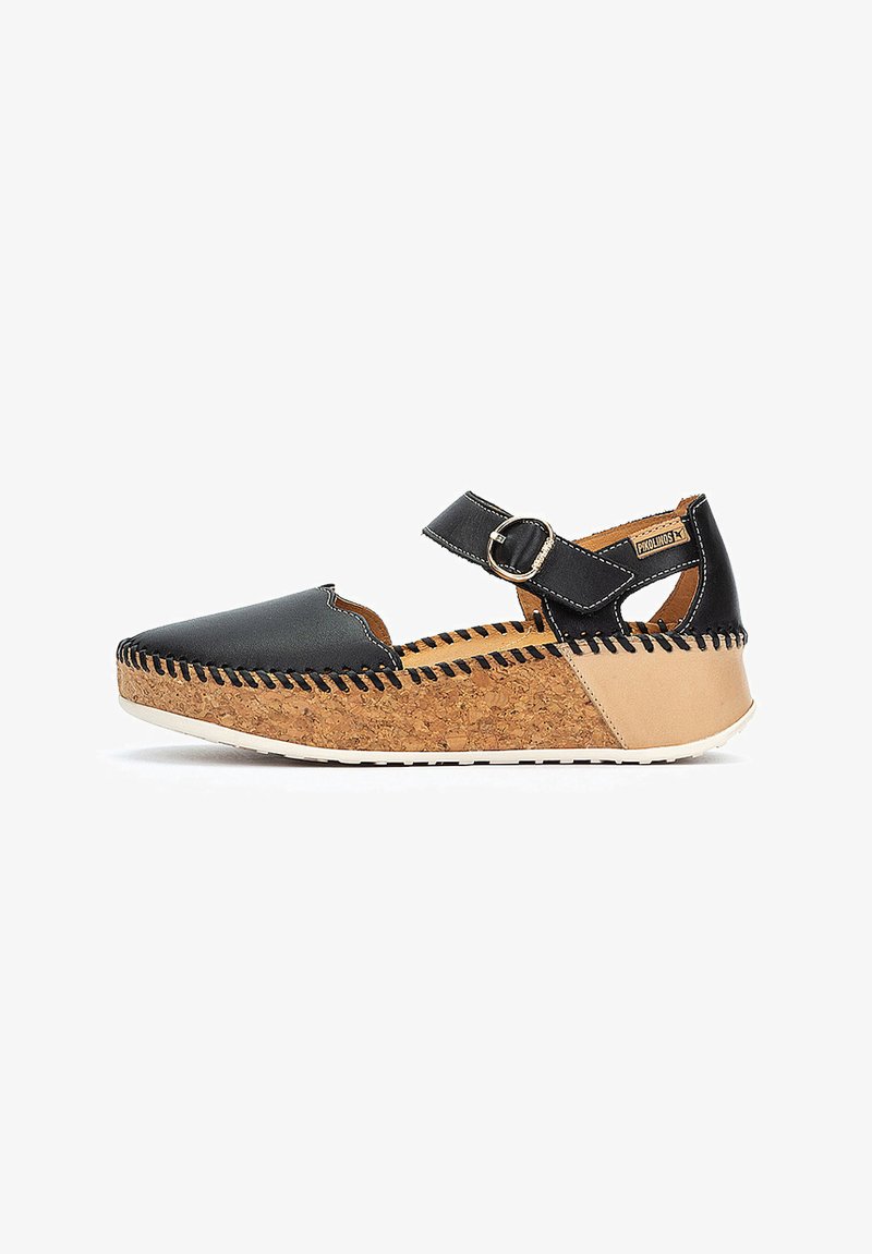 Zapato de cuero negro con una suela de plataforma de corcho, que presenta una puntera redonda y una correa ajustable con un hebilla metálica. Los detalles de costura acentúan el diseño.