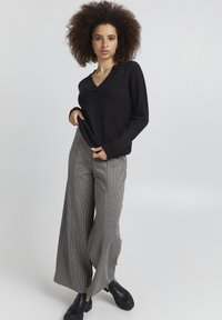 Adīta melna jakas ar V veida kakla izgriezumu, kombinēta ar platām pelēkām raibām biksēm. Melni masīvi zābaki noslēdz tēlu.