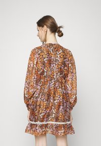 Vestido fluido e floral com um estampado multicolorido em material transparente. Apresenta mangas longas, bainha com babados e um acabamento decorativo em renda branca.