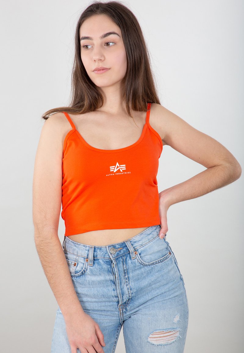 Top court orange vif à fines bretelles avec un logo blanc centré sur la poitrine. Associé à un jean bleu clair taille haute.