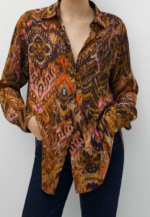 Chemise à coupe ample, boutonnée, à manches longues avec un motif abstrait marron, orange, violet et noir, portée avec un jean foncé.