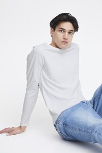 Hosszú ujjú fehér póló sima anyagból, kerek nyakkivágással. Világoskék farmernadrággal párosítva.