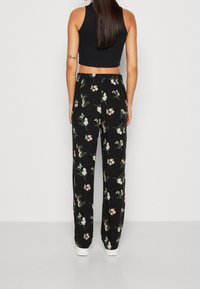 Pantalons floraux noirs à coupe ample, avec un motif de fleurs colorées et une taille élastique. Associés à un crop top noir ajusté.