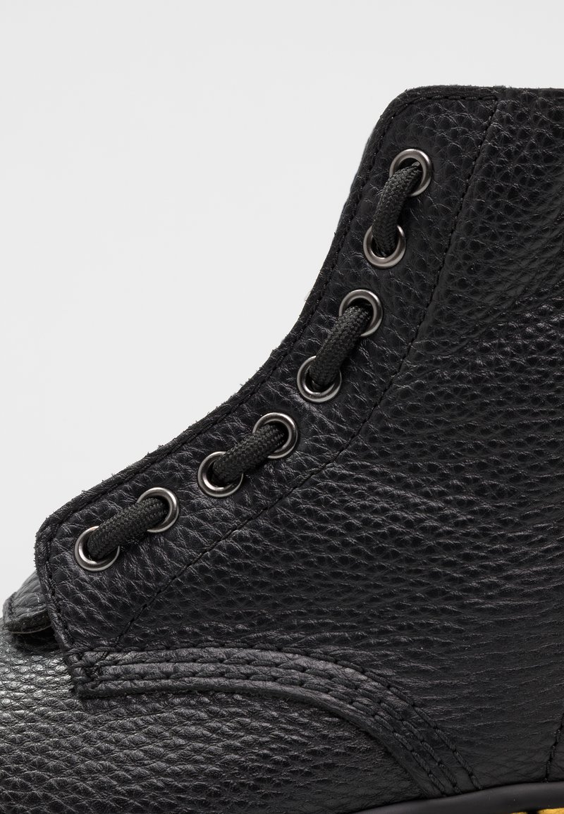 Black leather ankle boot featuring a textured finish, metal eyelets, and black laces, with a rounded toe and reinforced upper.