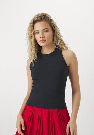 Čierny bezrukávový top s vysokým výstrihom, vyrobený z elastického materiálu, v súlade s červenou plisovanou sukňou. Hladká textúra, priliehavý strih.