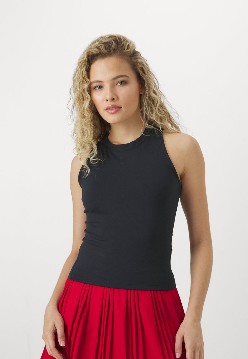 Črna brezrokavnica z visokim izrezom, izdelana iz raztegljive tkanine, v kombinaciji s kratko rdečo plisirano krilo. Gladka tekstura, prilagojen dizajn.