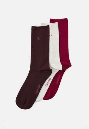 Three pairs of socks: one solid burgundy, one heather grey, and one deep red. Made of soft material, featuring "Calvin Klein" logo in contrast.