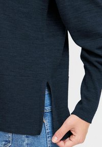 Temno modra pletena jopica z dolgimi rokavi, rebrastimi manšeti in stranskimi razporki na robu. Material ima gladko teksturo in subtilen vzorec.
