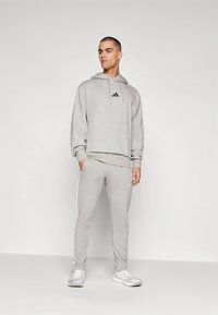 Γκρι αθλητική μπλούζα με κουκούλα, με μπροστινή τσέπη και λογότυπο, σετ με ταιριαστά παντελόνια φόρμας που διαθέτουν λευκές πλαϊνές ρίγες και στενή εφαρμογή.