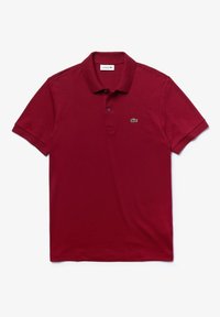 Czerwony bawełniany polo z krótkim rękawem, płaskim kołnierzykiem i trzema guzikami; posiada zielone logo Lacoste na lewej piersi.