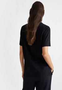 T-shirt nera a maniche corte realizzata in un tessuto liscio, con una vestibilità comoda e un collo rotondo. Design minimalista senza pattern visibili.