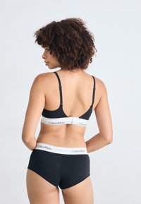 Black bralette and high-waisted panties with white waistband. Smooth fabric, adjustable straps, logo on waistband.
