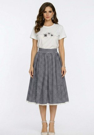 Femme portant un t-shirt blanc avec un motif floral noir, rentré dans une jupe midi à carreaux noir et blanc taille haute avec un bord en dentelle.