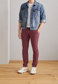 Veste en denim bleu clair, t-shirt blanc, pantalon bordeaux et baskets blanches avec des accents beige. Comprend des poches et des manches retroussées.