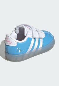Brosse de sport bleue et blanche en matériaux synthétiques. Comprend trois rayures blanches, des sangles en Velcro et une semelle en caoutchouc translucide avec des paillettes.