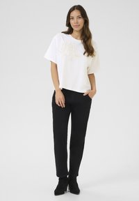 T-shirt blanc à manches courtes avec broderies florales, associé à un pantalon noir et des bottines. Design simple, coupe décontractée et combinaison de couleurs unie.