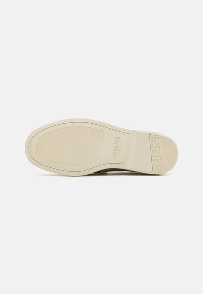 Shoe sole with a textured cream rubber material, featuring slight grooves and a raised logo. Curved edge and geometric pattern accent.