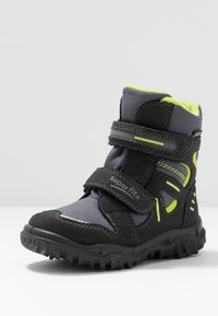 Stivaletto nera e grigia con accenti verde lime, realizzato in materiali tessili e sintetici, dotato di una fascia in velcro e suola texturizzata.