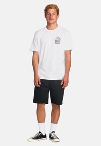 White cotton t-shirt with a graphic featuring palm trees, paired with black shorts and black sneakers. Plain white socks visible.