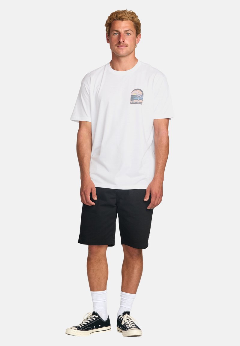 White cotton t-shirt with a graphic featuring palm trees, paired with black shorts and black sneakers. Plain white socks visible.