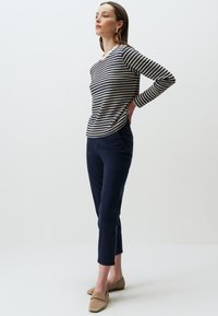 Gestreepte lange mouwen top in crème en marineblauw, gecombineerd met marineblauwe broek. Model draagt beige instapschoenen; soepele texturen en aansluitend ontwerp.