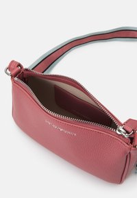 Růžová kožená kabelka s texturovaným povrchem. Má stříbrný zip a nastavitelný popruh s kontrastním pruhem.