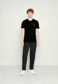Black cotton v-neck t-shirt with a small triangular logo, paired with dark pants and white sneakers, full front view against a light background.