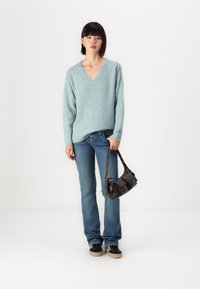 Pull-over en v bleu clair en maille texturée, jean foncé, baskets noires avec semelles en tan, et un petit sac à main marron avec une courte bandoulière.