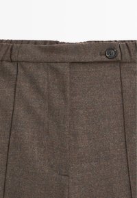 Hnědé tvídové kalhoty s záhyby, elastickým pasem a knoflíkovým zapínáním. Tkanina je měkká a lehce texturovan�á.