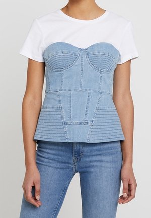 Jeansowy gorset z dopasowanym gorsetem, niebieskim odcieniem i pionowymi szwami, zestawiony z prostą białą koszulką i niebieskimi dżinsami.