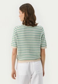 Sweter w paski, wykonany z dzianiny, w jasnym zielonym i kremowym kolorze, z krótkimi rękawami, okrągłym dekoltem i ściągaczem u dołu. Noszony z białymi spodniami.