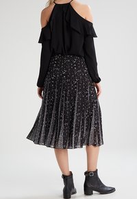 Top nero senza spalle con dettagli a volant abbinato a una gonna nera plissè con motivi floreali bianchi, completato da stivaletti neri alla caviglia.