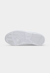 Semelle en caoutchouc blanche avec motifs zigzag et géométriques texturés, avec le nom de la marque Lacoste embossé au centre.