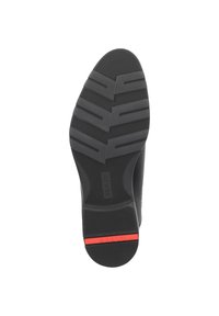 Suela de zapato de goma negra con un patrón de banda de rodadura en zigzag, que presenta una ranura circular central y un acento rojo cerca del talón.
