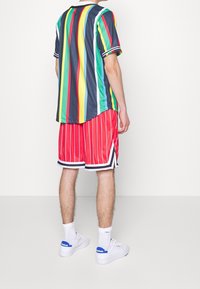 Meerlagig gestreept shirt met korte mouwen in blauw, groen, geel, rood en zwart. Gecombineerd met rood gestreepte korte broek en witte sneakers.