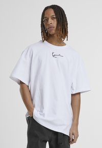 T-shirt en coton oversize blanc avec un logo noir brodé sur la poitrine. Manches courtes et coupe décontractée avec un col rond.
