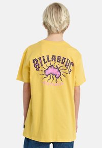 Geel katoenen T-shirt met een grote grafiek van Australië met een zonnestraalontwerp en de tekst "Billabong" in paarse en zwarte letters op de rug.