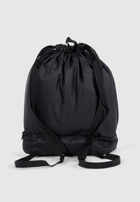 Drawstring backpack made of black, textured fabric with a hexagonal pattern, featuring adjustable straps and a zippered compartment at the base.