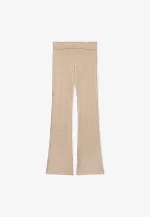 Leggings beige a zampa d'elefante realizzati in un tessuto morbido. Presentano una vita ampia ed elastica e una silhouette slanciata con una gamba inferiore a zampa.