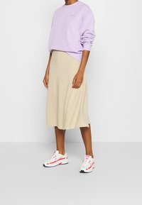 Sudadera lila con mangas enrolladas, falda midi beige y zapatillas blancas con detalles en rosa y naranja. Texturas suaves en todo.