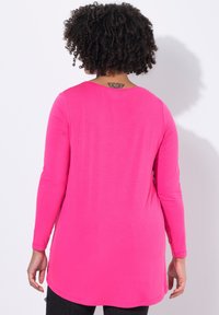 Langärmliges, pinkes Tunika-Top mit rundem Ausschnitt. Glatte Textur und geschwungener Saum. Bietet einen lockeren Schnitt und reicht bis unter die Hüfte.